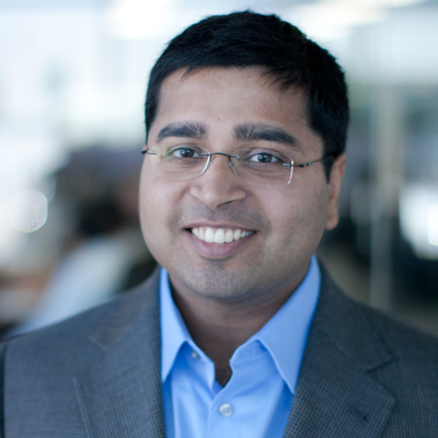 Manav Mital, CEO of Cyral, has dark eyes and hair and wears rimless glasses, a blue button-down shirt, and gray jacket