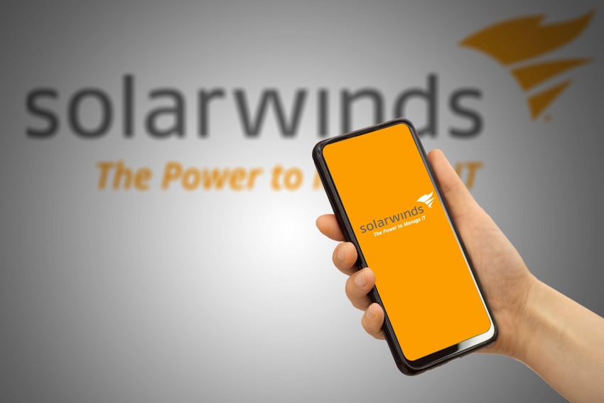 Hand holding a cellphone with SolarWinds logo on screen, and another SolwarWinds logo in background