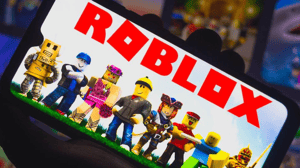 Roblox logo and various gaming characters displayed on a mobile device screen held in someone's hand Roblox logo and various gaming characters displayed on a mobile device screen held in someone's hand