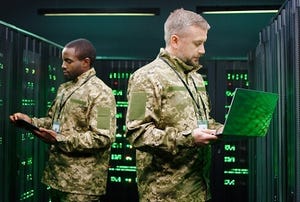 Picture of two men in green camouflage military uniforms standing in a server room inspecting the equipment.