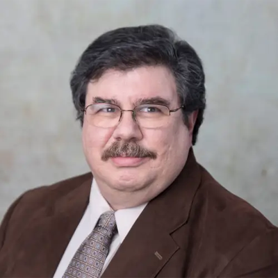 Stephen Lawton has short dark hair and a mustache; he wears wire glasses and a suit with tie.