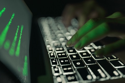 Person typing on a laptop in a darkened room with green code on the screen