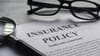 An insurance policy on paper next to glasses and a magnifying glass. An insurance policy on paper next to glasses and a magnifying glass.