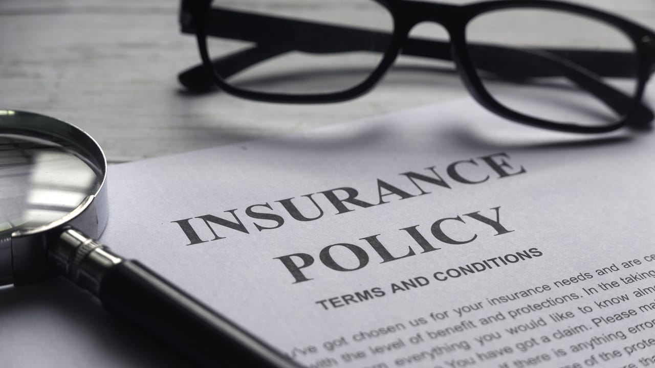 An insurance policy on paper next to glasses and a magnifying glass. An insurance policy on paper next to glasses and a magnifying glass.