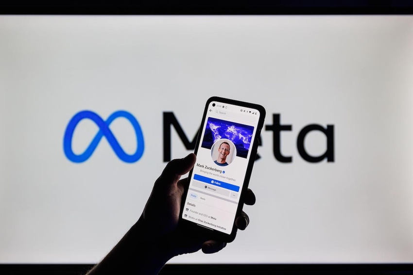 Hand holding a cellphone with Facebook on it, in front of Meta logo in background