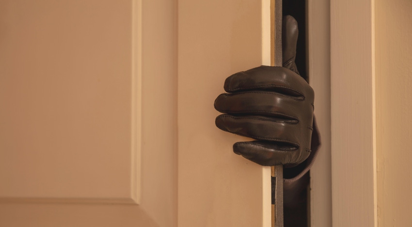 An intruders gloved hand clasped around the edge of a door.