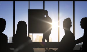 Silhouettes of individuals sitting in a boardroom with one giving a presentation