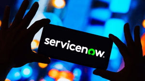 Hands in a shadow against blurred bright colored lights holding a device with "servicenow" displayed on the screen Hands in a shadow against blurred bright colored lights holding a device with "servicenow" displayed on the screen