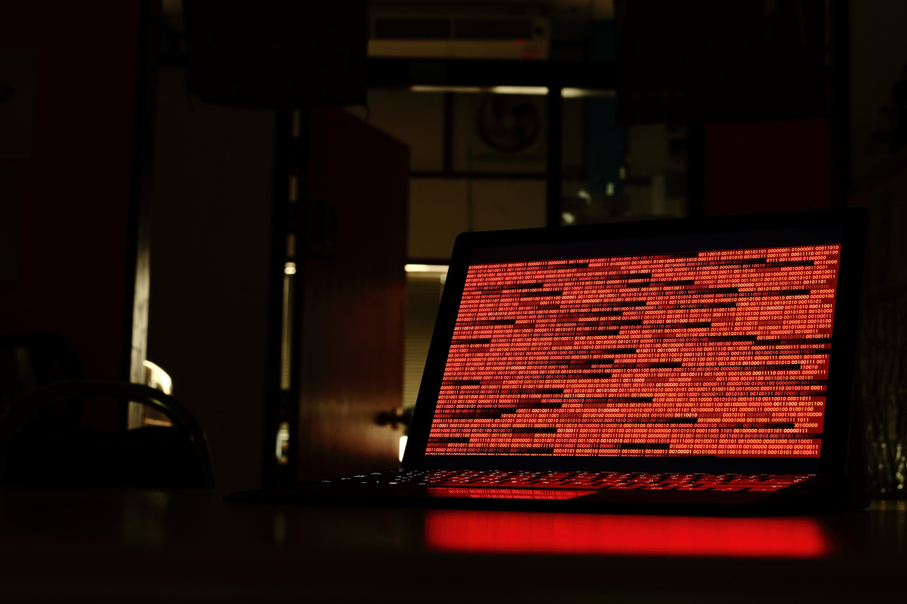 an image of a laptop screen in a dark room, with compromised red code all across the screen. an image of a laptop screen in a dark room, with compromised red code all across the screen.