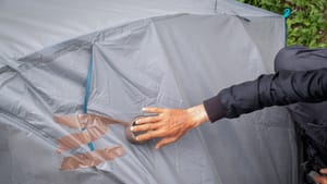 A hand reaching to tape up hole in a tent. A hand reaching to tape up hole in a tent.