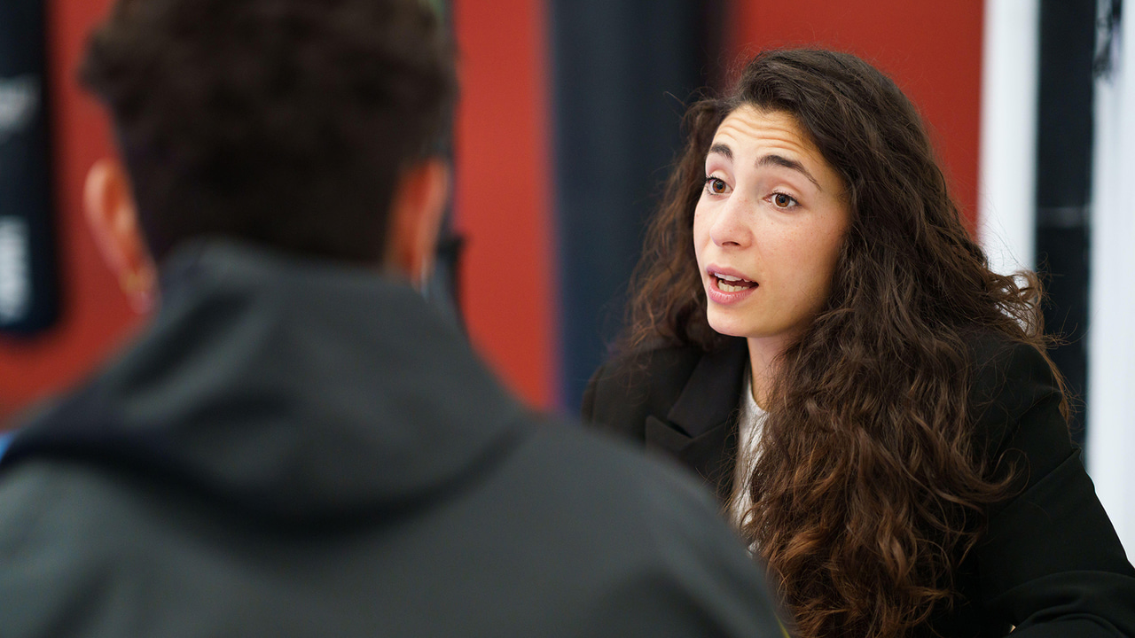A curly haired woman speaking to another person who we see only the back of the head A curly haired woman speaking to another person who we see only the back of the head
