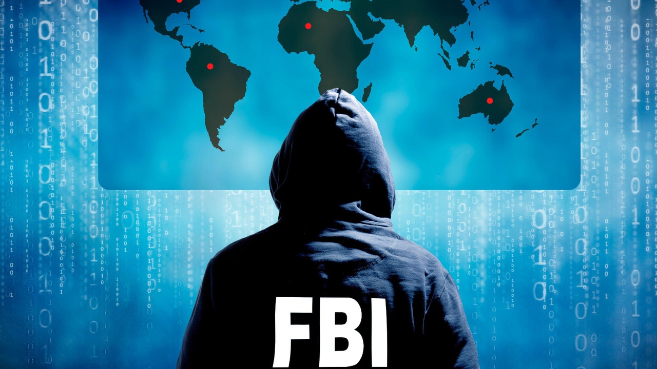 Person with their back to the camera in hooded sweatshirt with FBI on the back facing a flat map of the world with red dots marking various locations Person with their back to the camera in hooded sweatshirt with FBI on the back facing a flat map of the world with red dots marking various locations