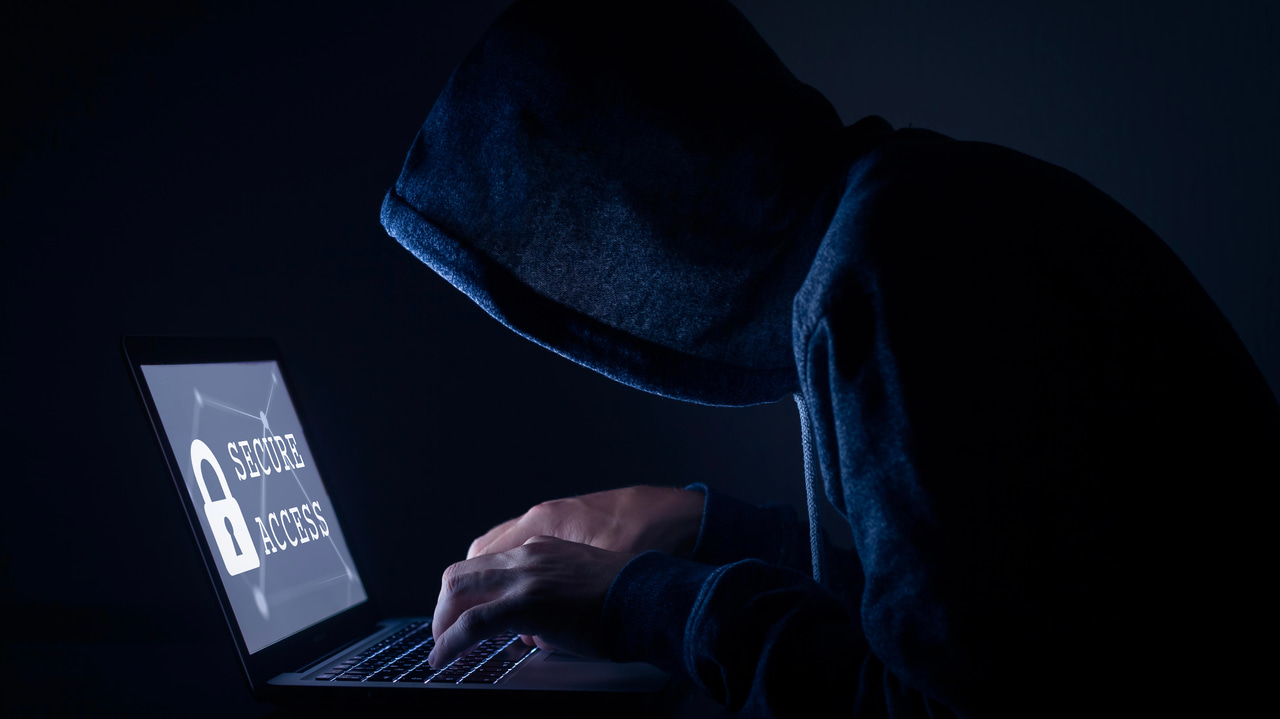 暗い部屋でノートパソコンを操作するフードをかぶったハッカー。画面にはロックが表示され、「Secure Access」と書かれている 暗い部屋でノートパソコンを操作するフードをかぶったハッカー。画面にはロックが表示され、「Secure Access」と書かれている
