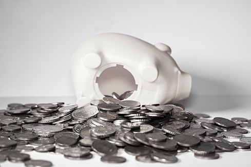 a white piggy bank open at the bottom with a bunch of coins spilling out.