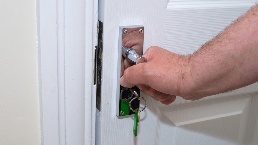 A man opens a door with a key hanging from the lock