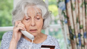 An elderly woman talking on the phone while holding a credit card