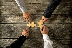 Four hands moving two puzzle pieces; suggestion of merger or creative cooperation of two businesses