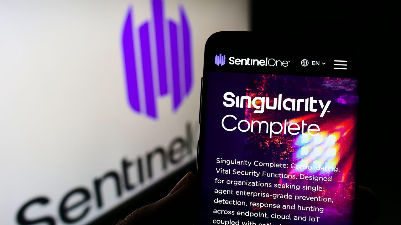SentinelOneのロゴを表示する画面と、その前景にSingularityのロゴを表示するスマートフォンの画面 SentinelOneのロゴを表示する画面と、その前景にSingularityのロゴを表示するスマートフォンの画面