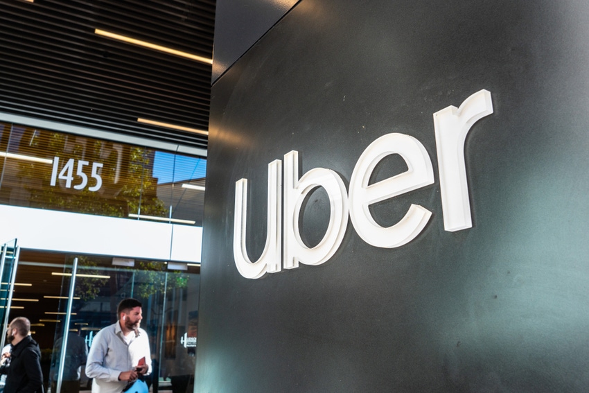 Photo contains image of Uber logo in corporate setting with man in the background