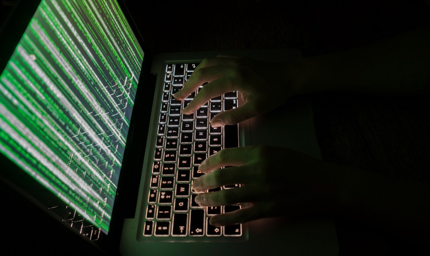 Hands type on a laptop keyboard in a dark room; code in green appears on screen