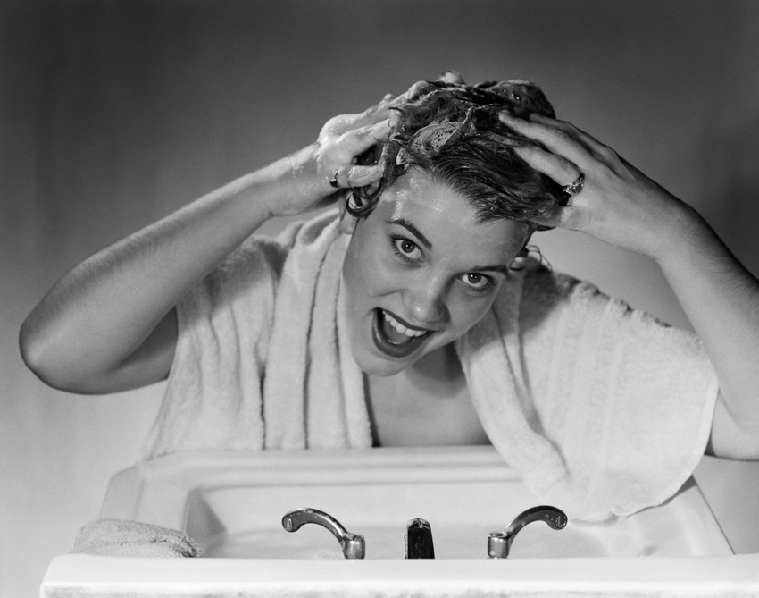 1950s SMILING WOMAN WASHING SHAMPOOING HAIR IN SINK LOOKING AT CAMERA
