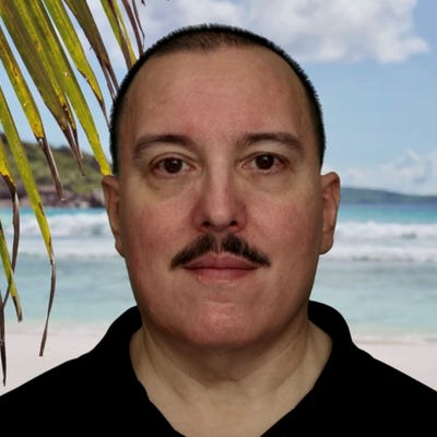 Roland Dobbins, Principal Engineer at Netscout, wears a mustache and a black polo shirt; he's standing on a tropical beach