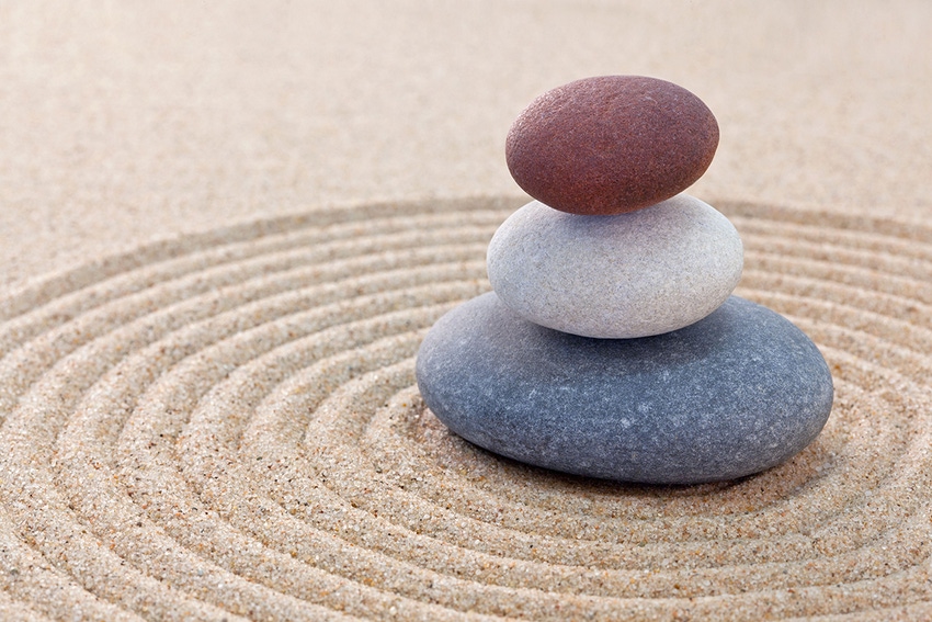 Three pebbles stacked on a circular raked Zen garden