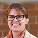 Kris Lovejoy wears tortoiseshell-framed glasses and a scarf. She is standing in front of a brick wall. Kris Lovejoy wears tortoiseshell-framed glasses and a scarf. She is standing in front of a brick wall.
