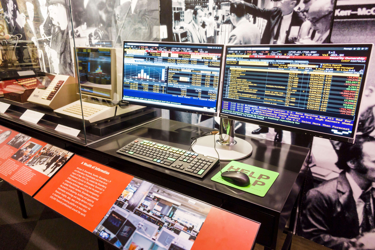 Bloomberg Terminal museum display, a plexiglass box with a terminal and two monitors showing a ton of financial data Bloomberg Terminal museum display, a plexiglass box with a terminal and two monitors showing a ton of financial data