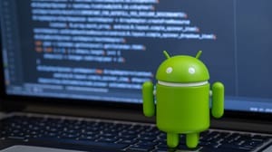 Google Android figure standing on laptop keyboard with code onscreen Google Android figure standing on laptop keyboard with code onscreen
