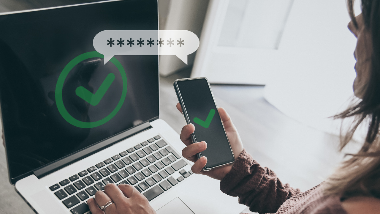 A woman sitting at a laptop and holding a mobile device, the screens of both displaying a green check mark in a circle A woman sitting at a laptop and holding a mobile device, the screens of both displaying a green check mark in a circle