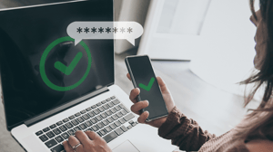 A woman sitting at a laptop and holding a mobile device, the screens of both displaying a green check mark in a circle A woman sitting at a laptop and holding a mobile device, the screens of both displaying a green check mark in a circle