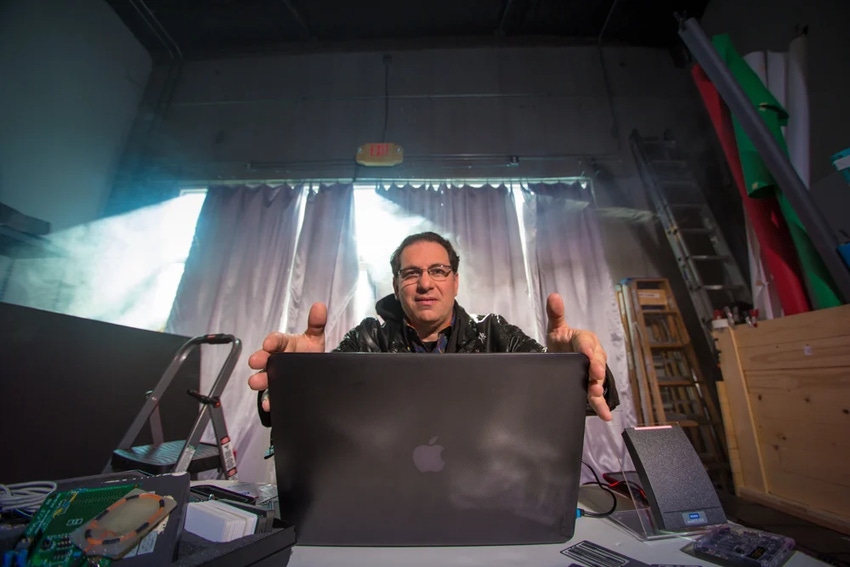Kevin Mitnick seated at a desk behind a laptop with light coming through the curtains behind him