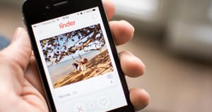 Mobile device in a hand with the Tinder app open to a profile Mobile device in a hand with the Tinder app open to a profile