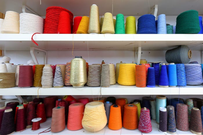 Cones and spools of colorful sewing thread organized by color from red, orange, yellow, blue