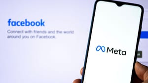 A phone with the meta logo on the screen held up in front of a background with the original Facebook login page A phone with the meta logo on the screen held up in front of a background with the original Facebook login page