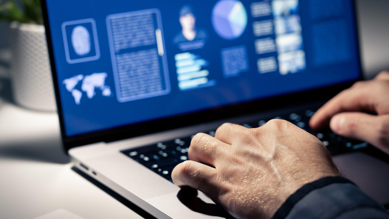 Police using computer; closeup of hands on keyboard, plus evidence documents and profile of crime suspect with photo on laptop screen Police using computer; closeup of hands on keyboard, plus evidence documents and profile of crime suspect with photo on laptop screen