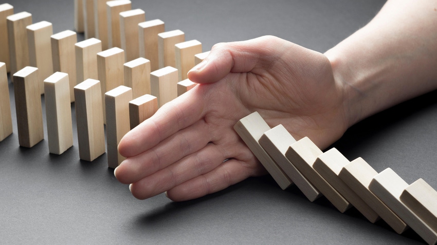 A hand comes in to block falling dominoes to set off three lines of upright dominoes
