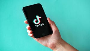 A person's hand in front of a turquoise background, holding a phone with the TikTok logo on the screen