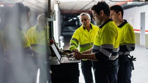 Three men in reflective jackets standing around a laptop Three men in reflective jackets standing around a laptop