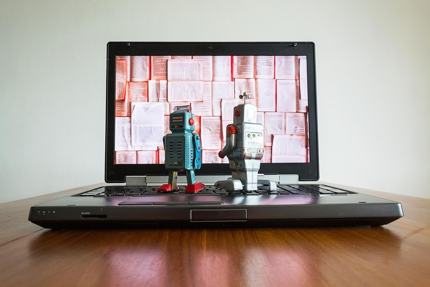 Photo of two toy robots standing on a laptop keyboard, staring at the display, which contains a layout of book pages