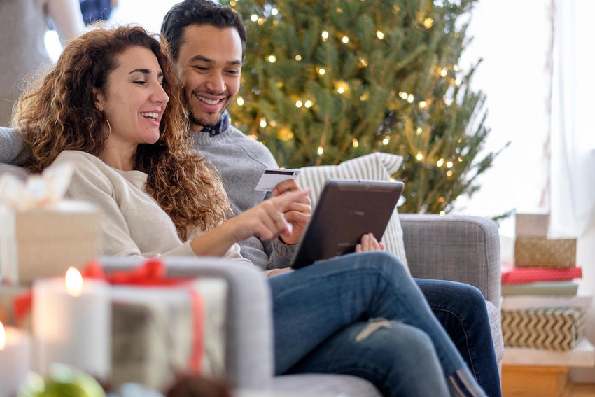 Couple sitting on a couch online-shopping on their tablet, with a Christmas tree in the background