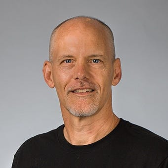 Allen Rogers has buzzed hair and slight groomed stubble; he has blue eyes and wears a black t-shirt