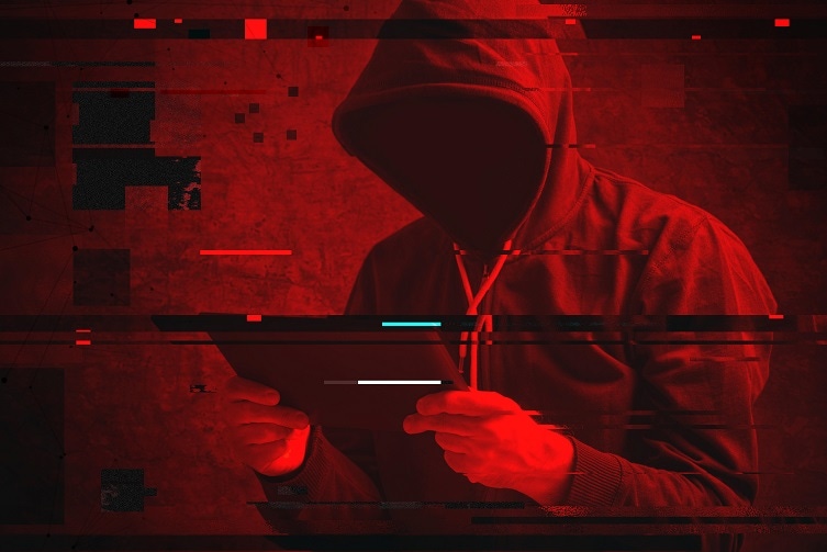 Person in hoodie holding a tablet device with their face obscured against a red background