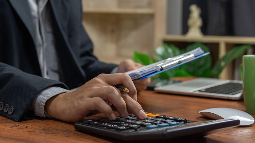 businessman doing finances on a calculator at his desk, with laptop in background