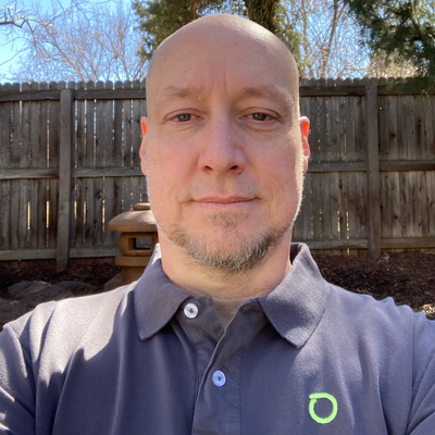 Andrew Green of Netscout has a shaved head and a short beard. He's wearing a company polo shirt in his pleasant backyard