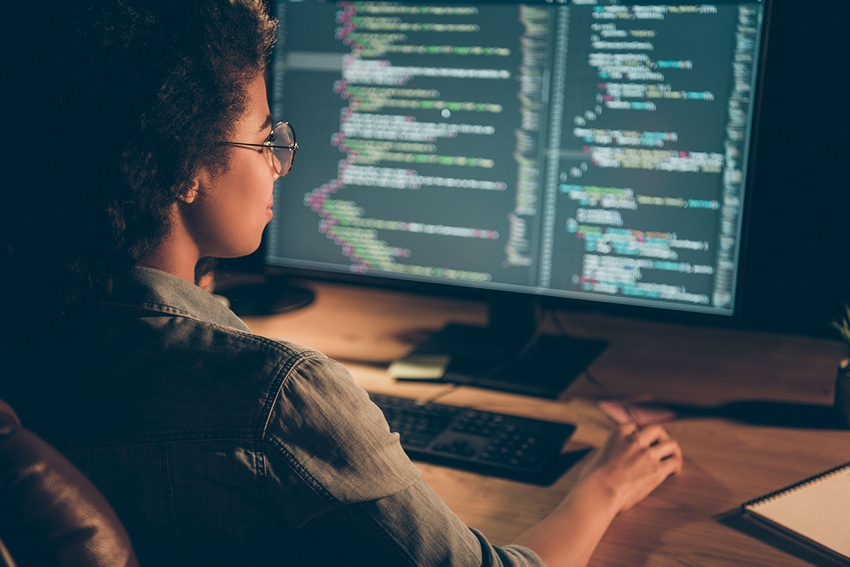 A young Black woman sits at a computer working on JavaScript code