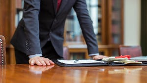 Man in suit leans over shiny desk with legal portfolio on it