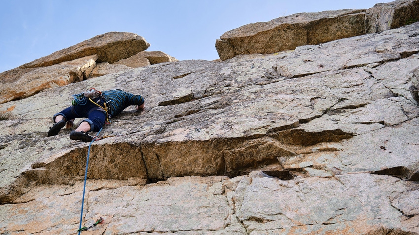 A person climbing a rock wall with climbing equipment and ropes on a sunny day
