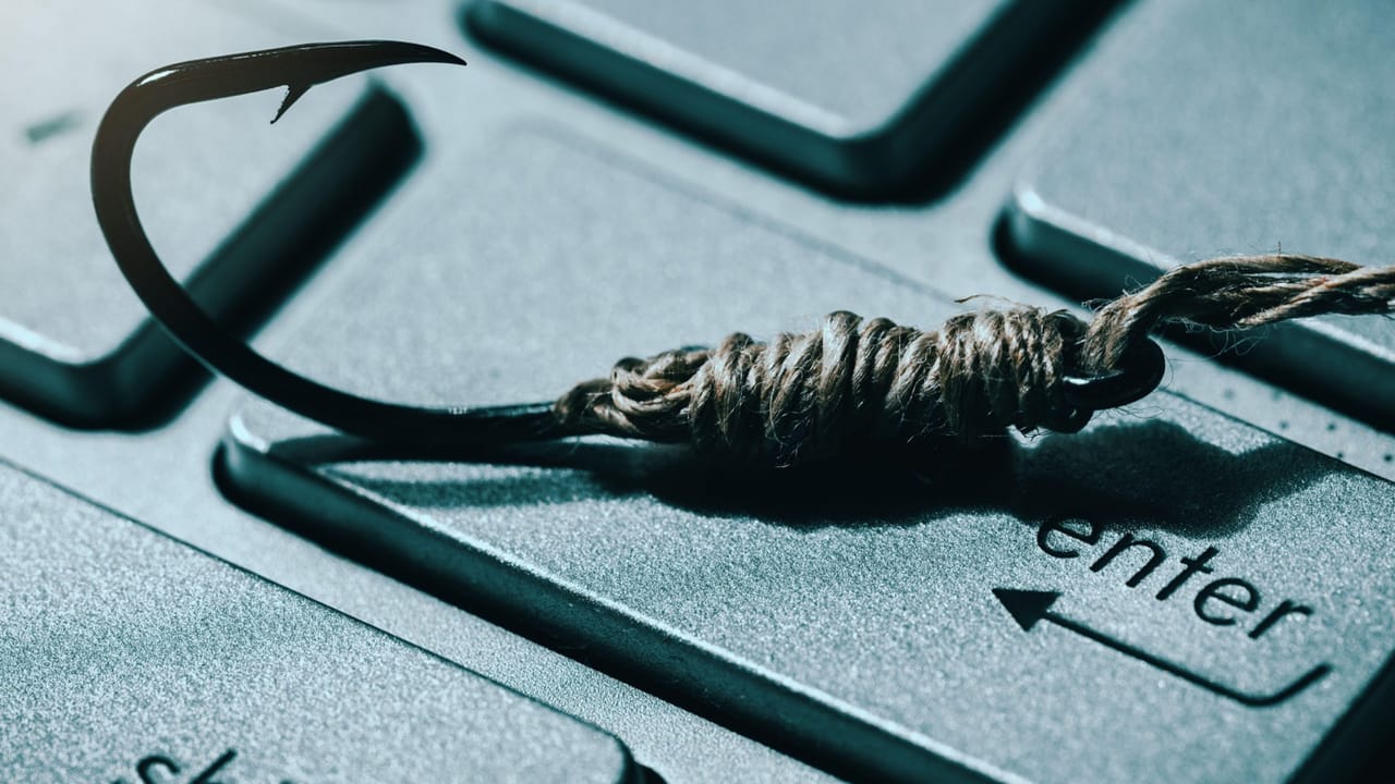 コードで巻かれた釣り針がコンピューターのキーボードの上に置かれている コードで巻かれた釣り針がコンピューターのキーボードの上に置かれている